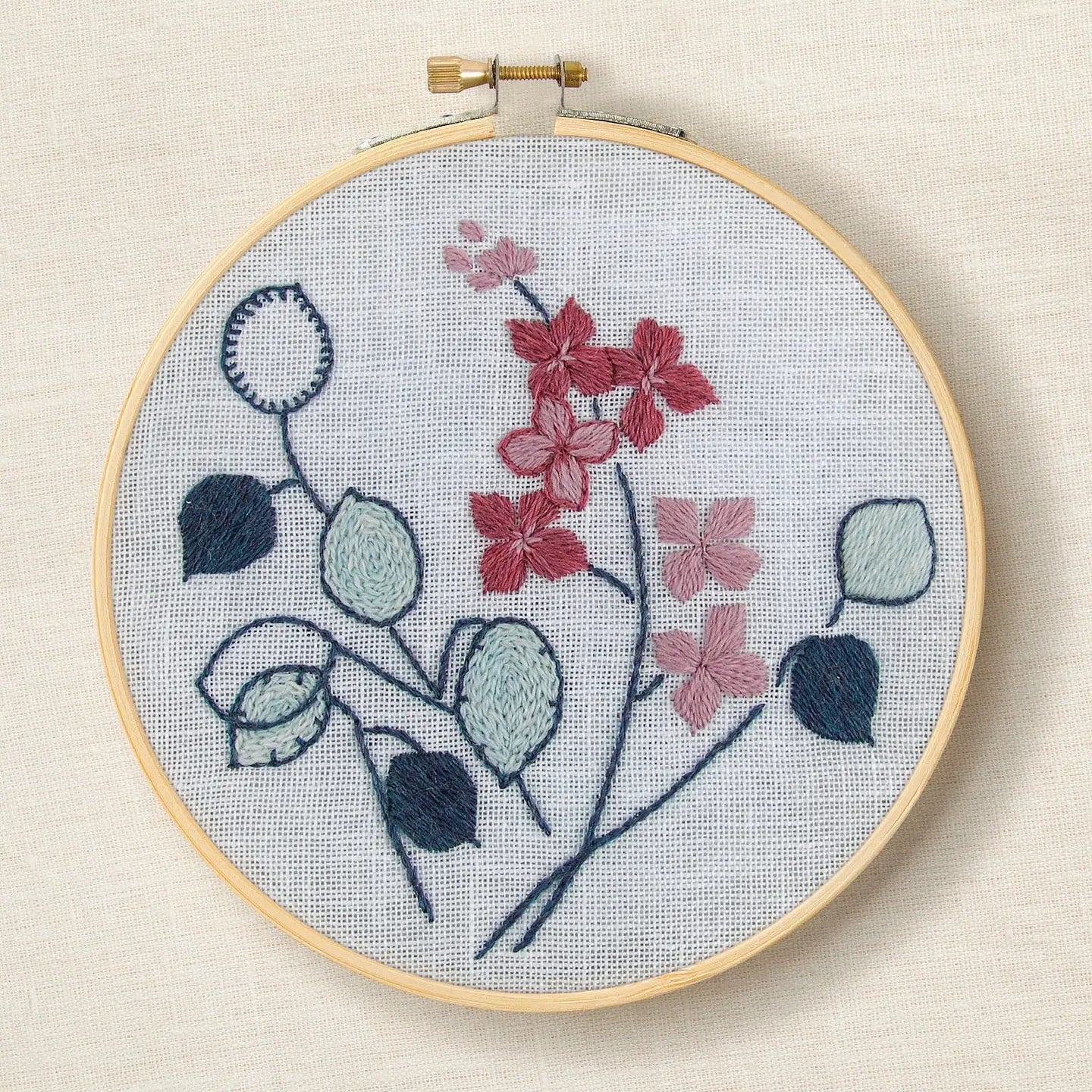 Embroidery hoop with botanical design in blue and pink tones on a light background