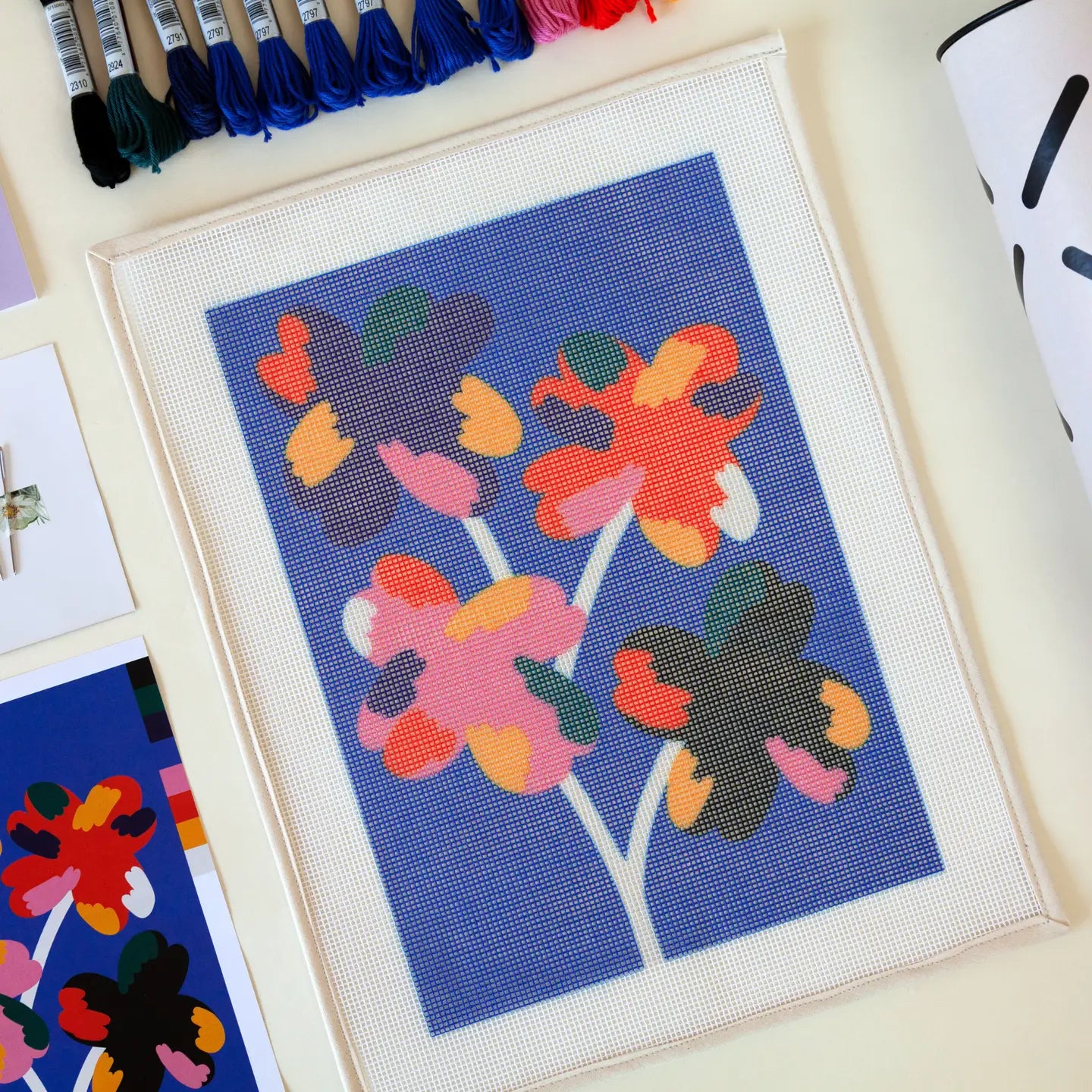 Close-up of some of the contents of a needlepoint kit with a vibrant Four Flowers abstract design, including a printed canvas and a variety of coloured threads