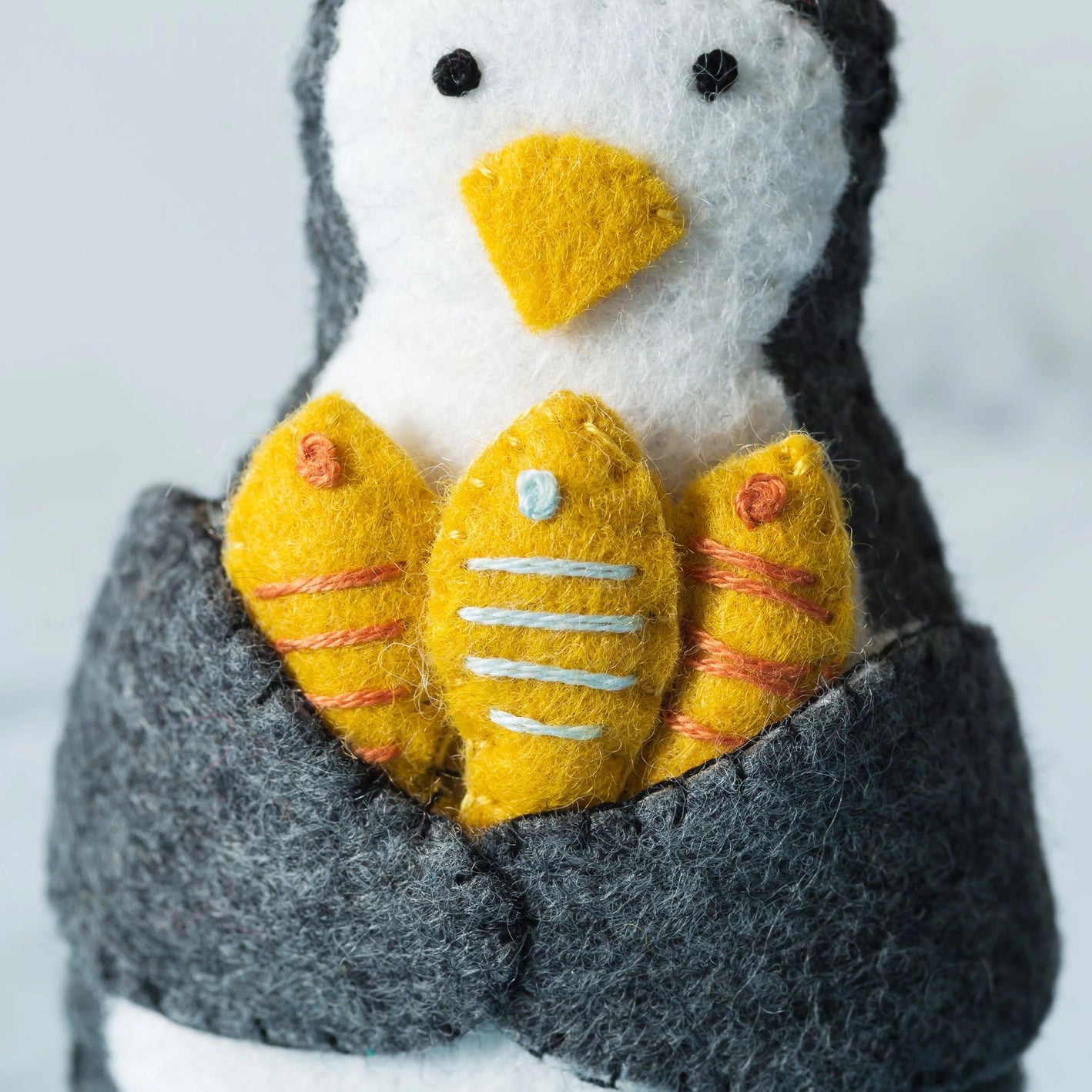 Close-up of a hand-stitched felt penguin decoration holding three fish