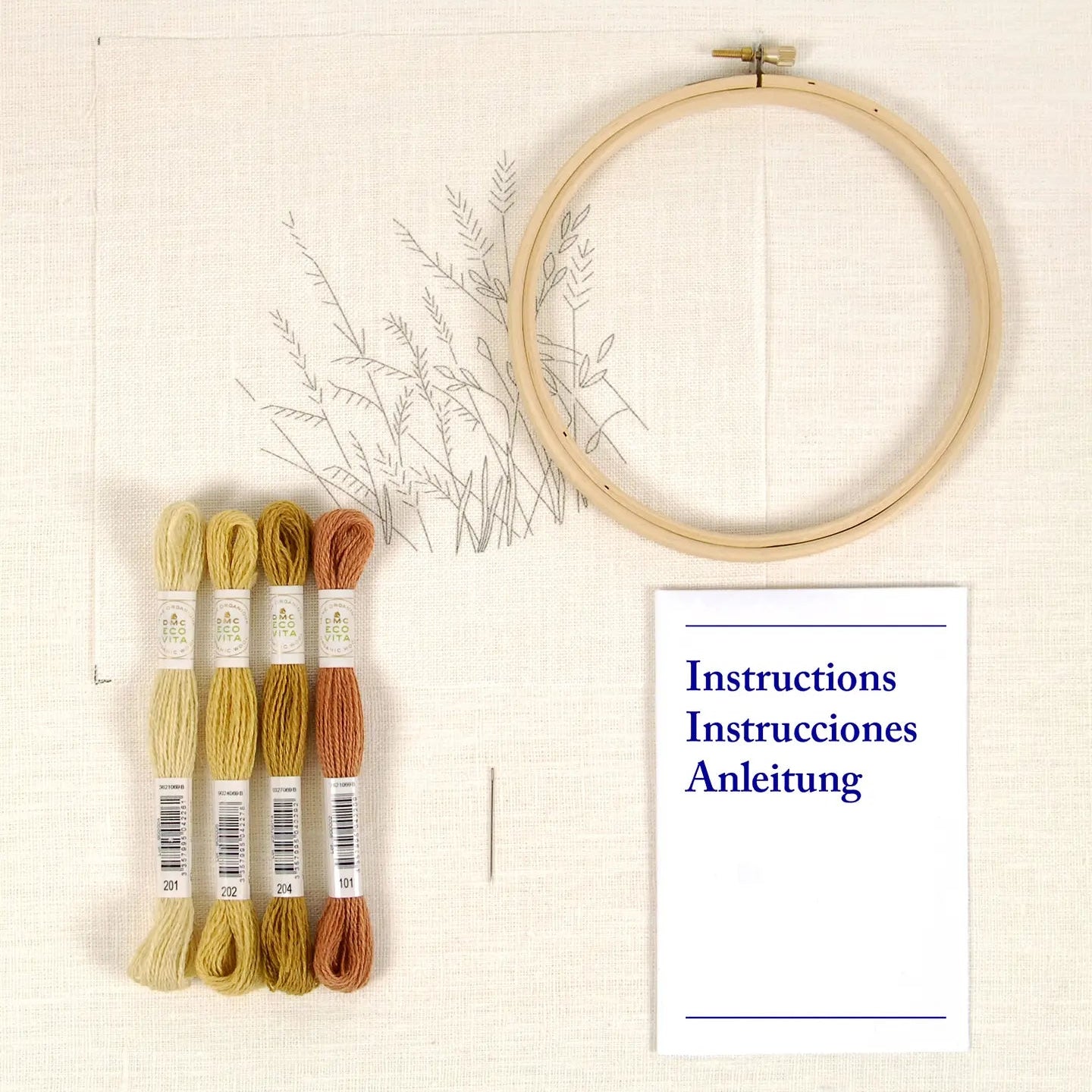Embroidery kit with printed fabric, bamboo hoop, colourful thread skeins, and an instruction booklet on a cream background.