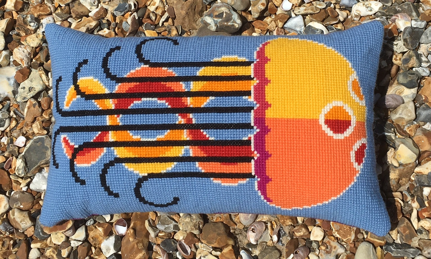 An Emily Peacock jellyfish cross stitch cushion placed on stones, available on mimosa store.
