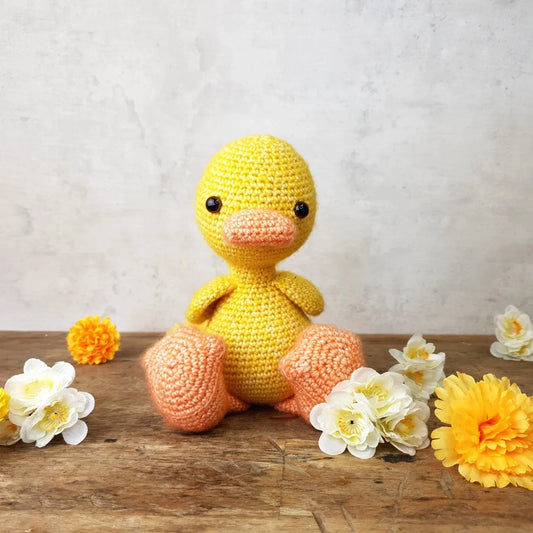 Crocheted yellow duck toy with flowers on a wooden surface