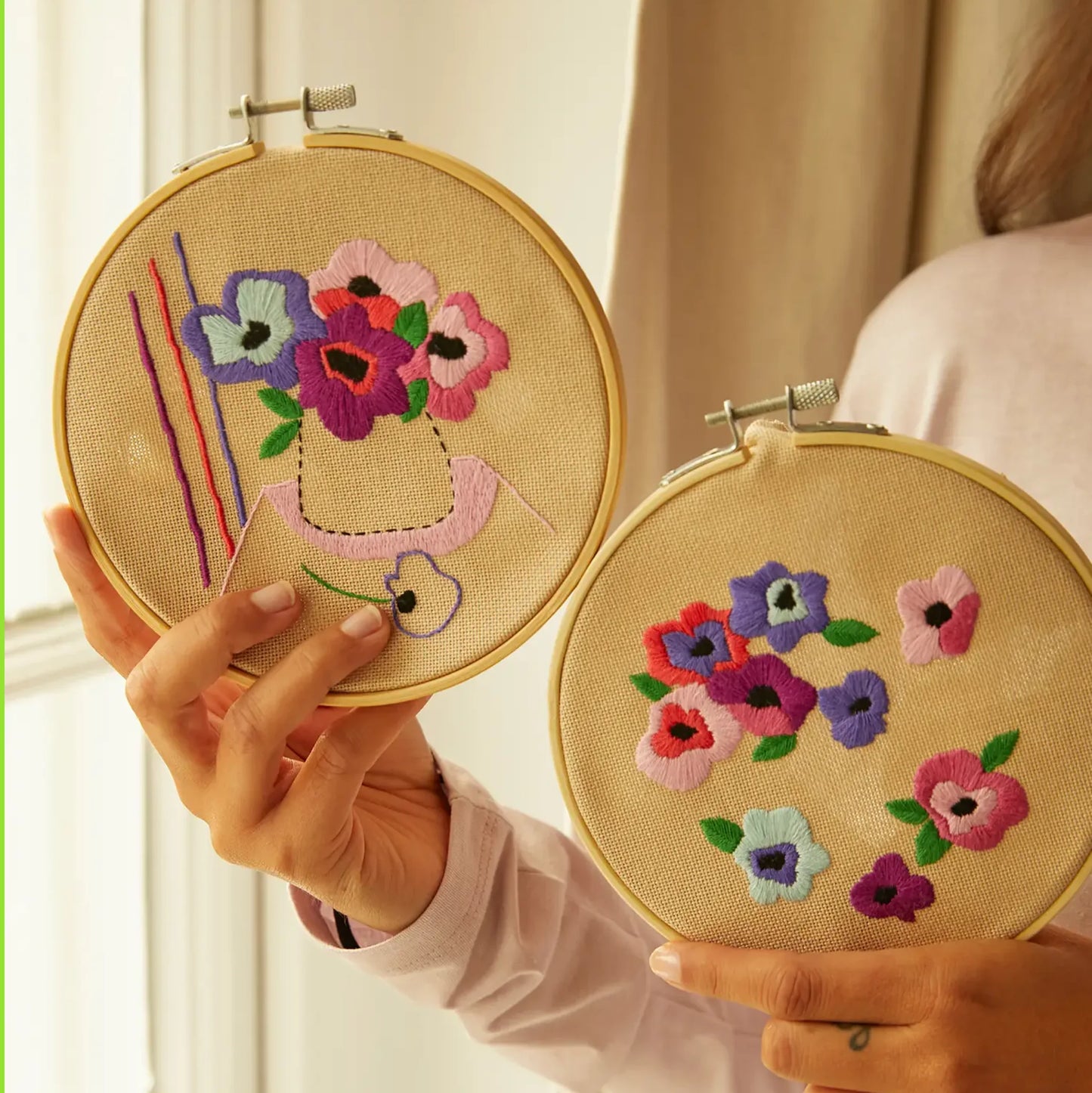 Person holding two completed coordinating floral embroideries in hoops
