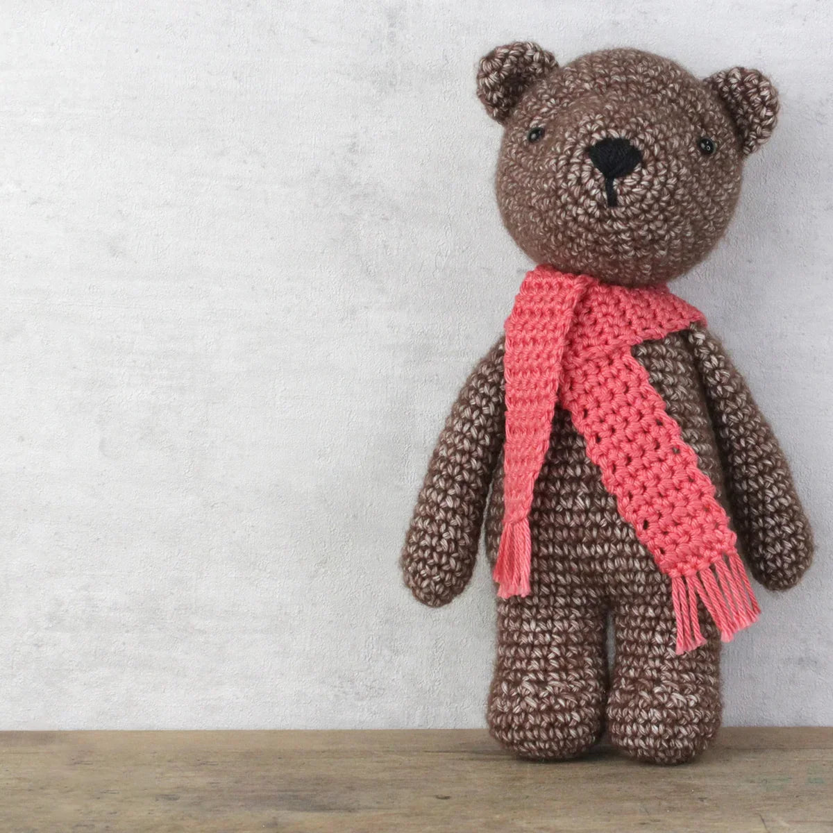 Brown teddy bear with a pink scarf on a wooden surface and light grey background
