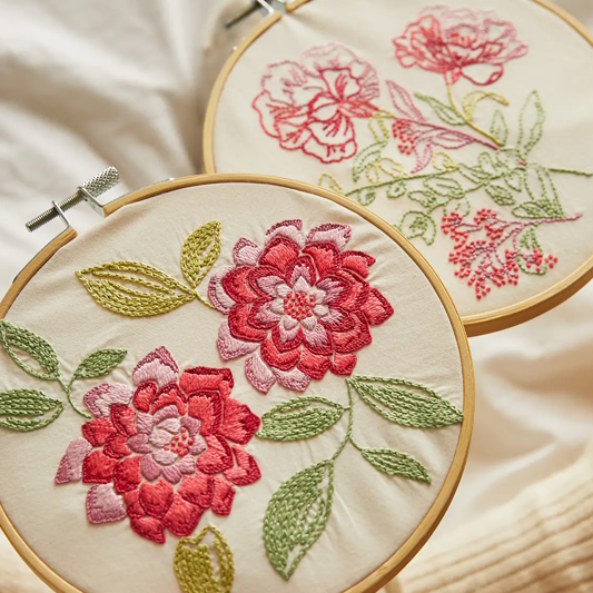 Two coordinating floral embroideries in hoops, featuring pink and green flowers on a cream background