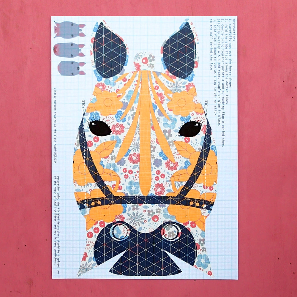 Close-up of one floral carousel horse paper decoration with yellow and blue highlights and instructions, on pink background
