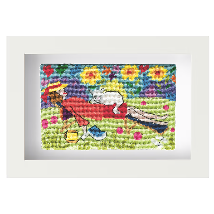 Colourful needlepoint postcard of a woman taking a catnap in the garden, with a white cat asleep on her, and a book and cup beside them, framed in white