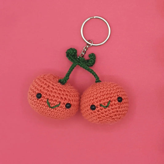 Crocheted cherries keychain or bag charm in shades of red and green on a pink background