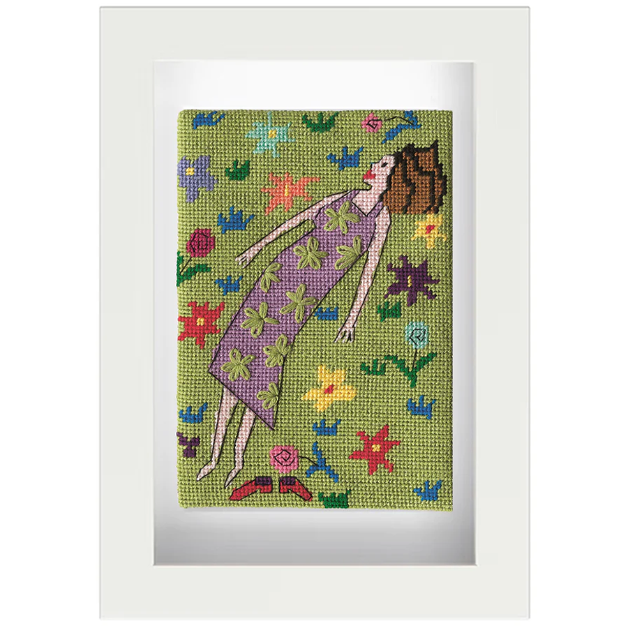 Needlepoint postcard of a woman lying in a colourful field watching clouds, on a green background, framed in white