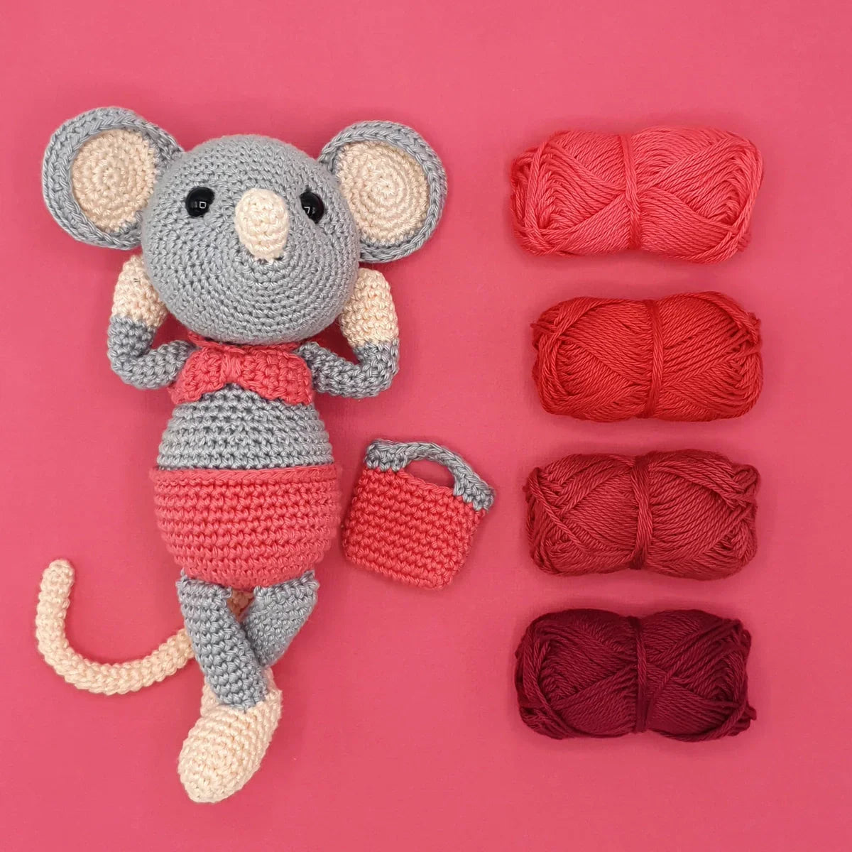 Crocheted mouse toy wearing a pink bikini, with a small matching bag and red yarn on a pink background