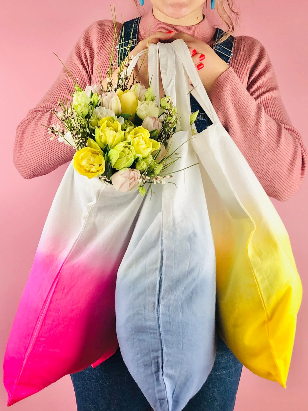 Person holding three dip dye tote bags in bright pink, blue and yellow colours