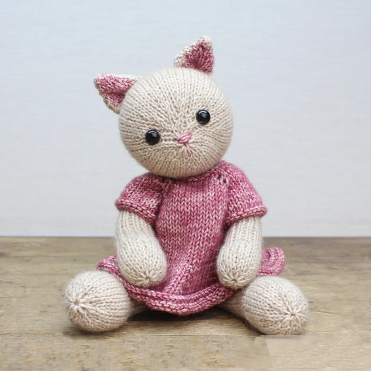 Knitted cat toy wearing a pink dress on a wooden surface with a light background