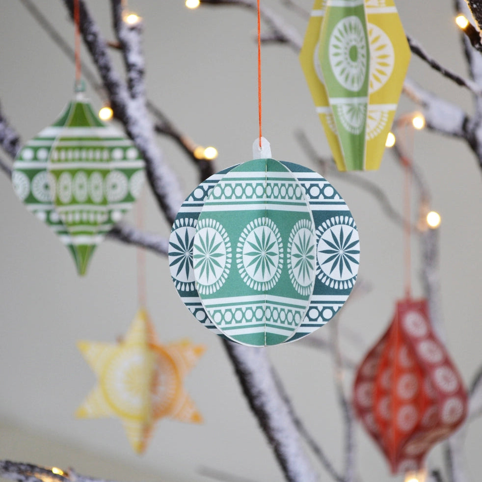 Printed paper Christmas decorations hanging from a branch, featuring brightly coloured geometric patterns