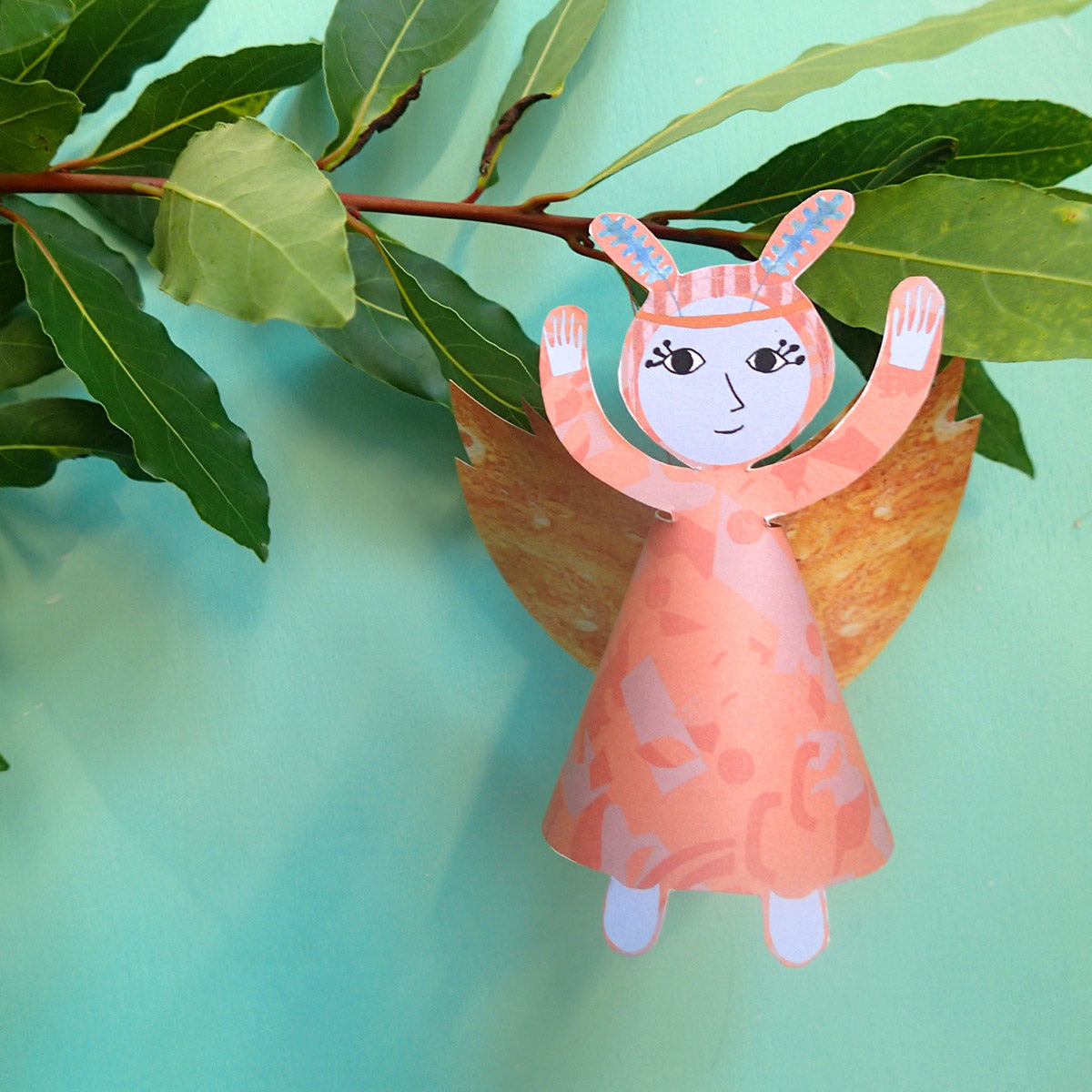 Close-up of finished orange festive fairy decoration with yellow wings and green leaf tiara on green background 