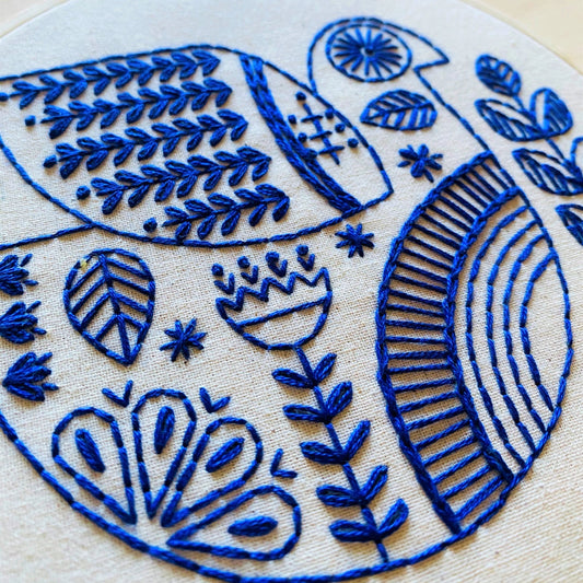 Close-up of a folk-inspired blue dove embroidery with decorative flowers and leaves on unbleached calico