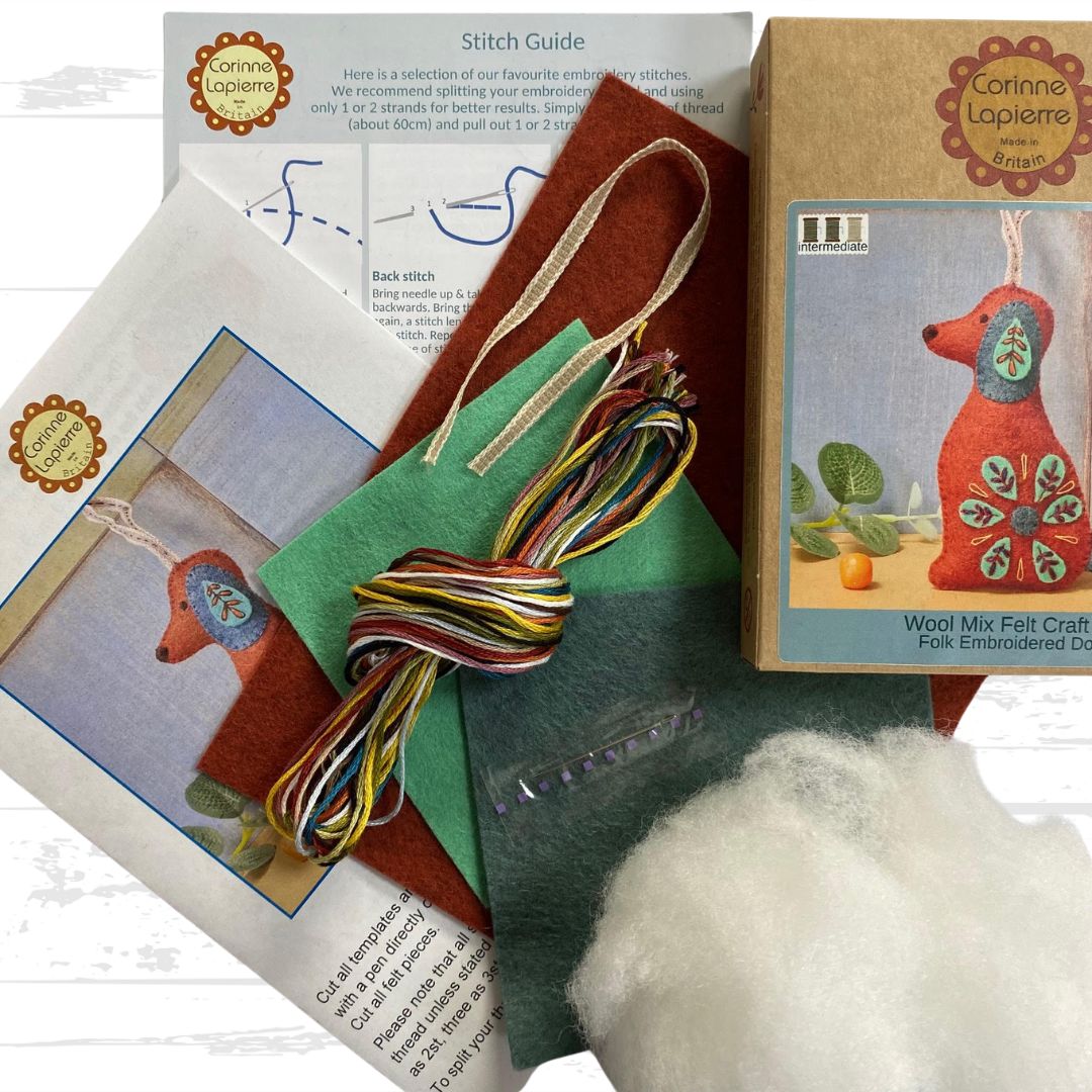 Contents of the folk embroidered dog felt craft kit, including packaging, felt pieces, embroidery floss, ribbon, toy filling, needle, and instruction booklet