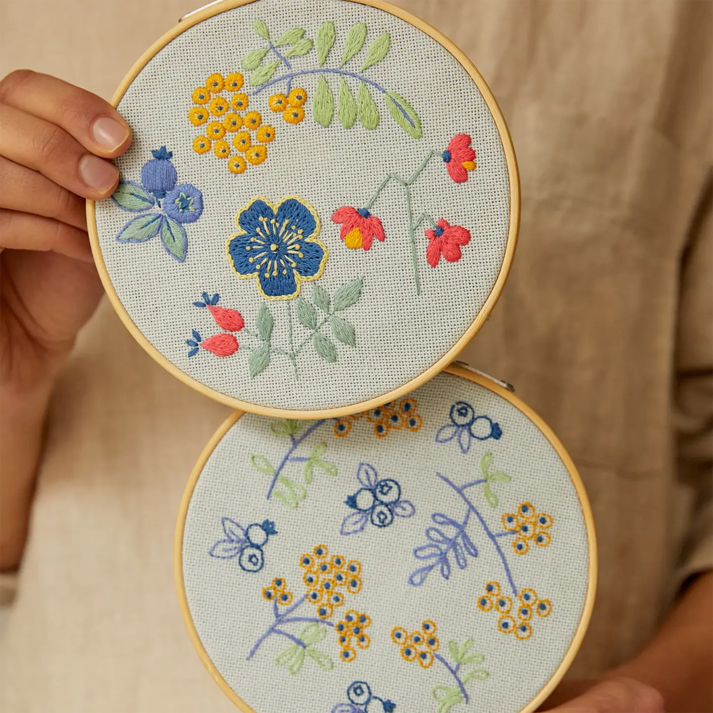 Two embroidered hoops with floral designs held by a person