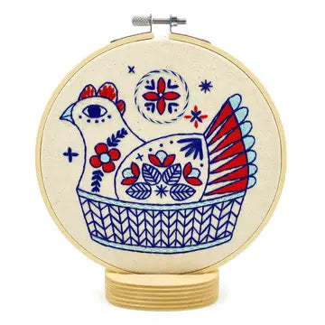 Finished embroidery of a red, white, and blue hen with floral details, sitting in a basket in a hoop