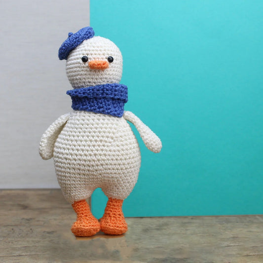 Crocheted goose toy with a blue hat and scarf against a teal background