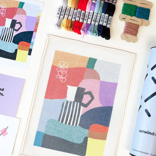 Close-up of some of the contents of a needlepoint kit with an abstract coffee-themed design, including a printed canvas  and a variety of coloured threads