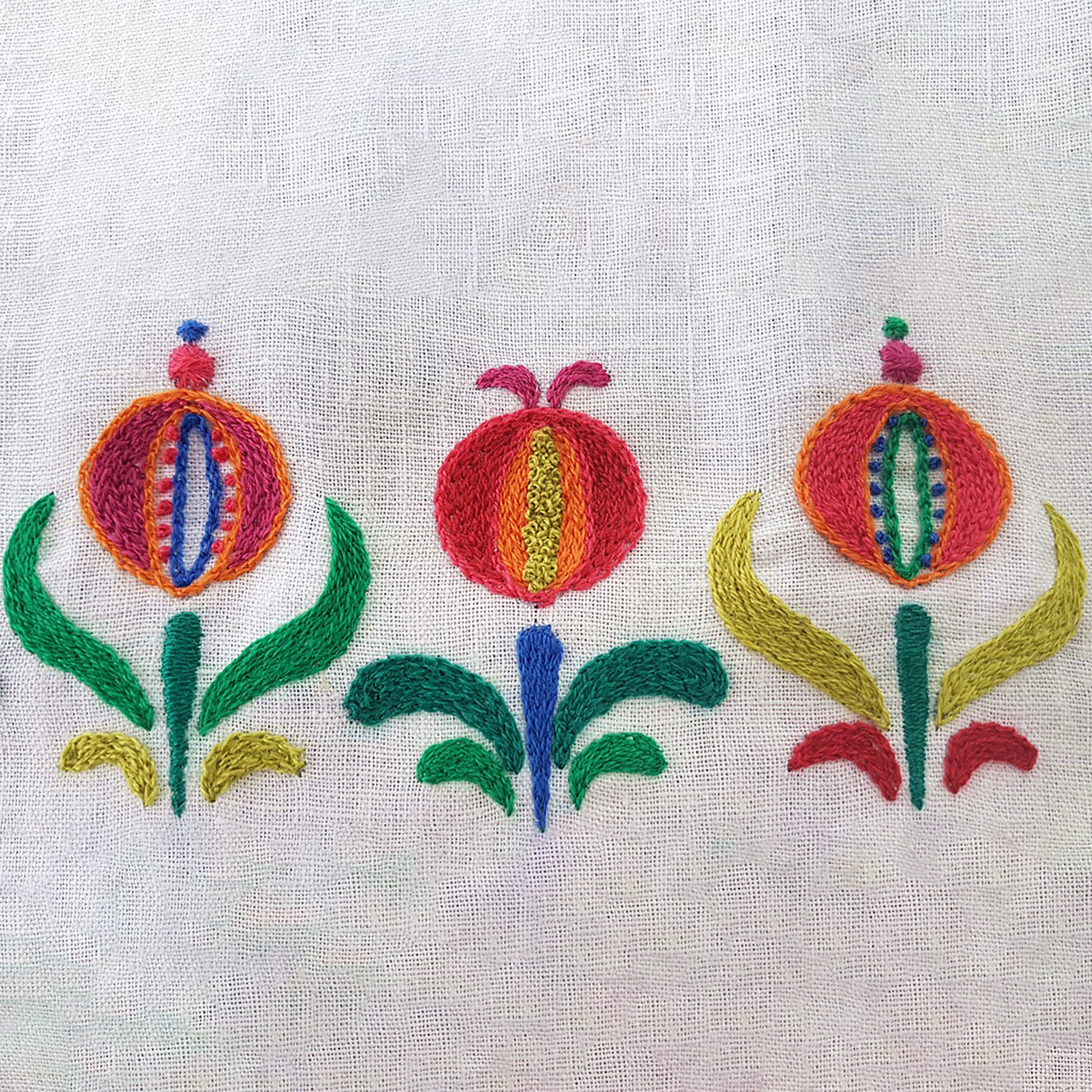 Close up of three embroidered pomegranate designs on an off-white fabric background