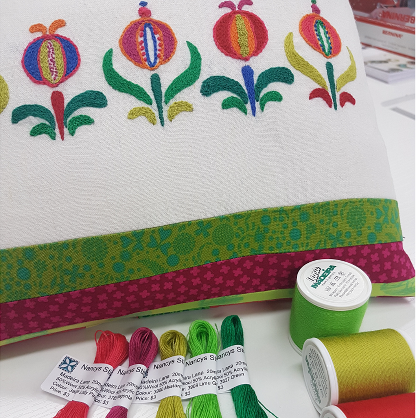 Embroidered cushion with floral design, featuring patchwork strips, with embroidery threads in the foreground