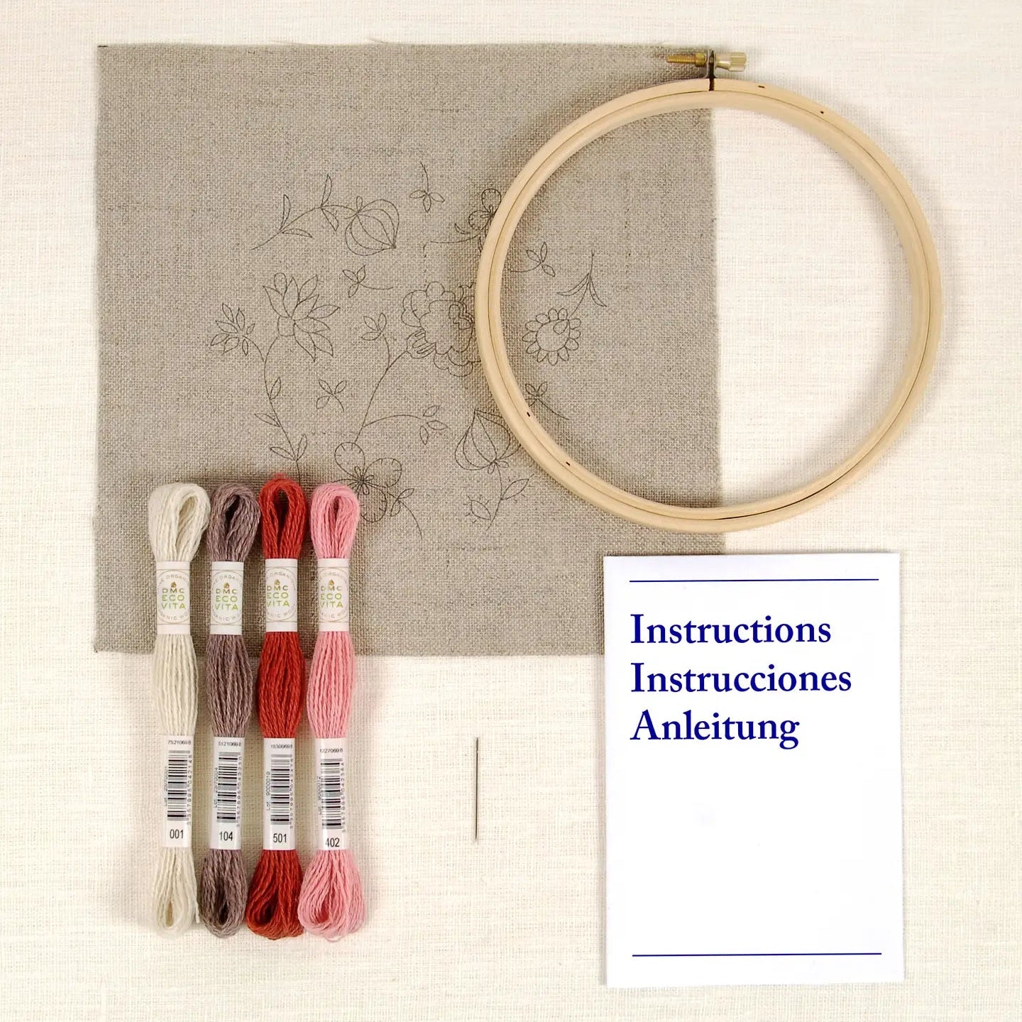 Embroidery hoop with fabric, threads, instruction sheet, and a needle on a light background