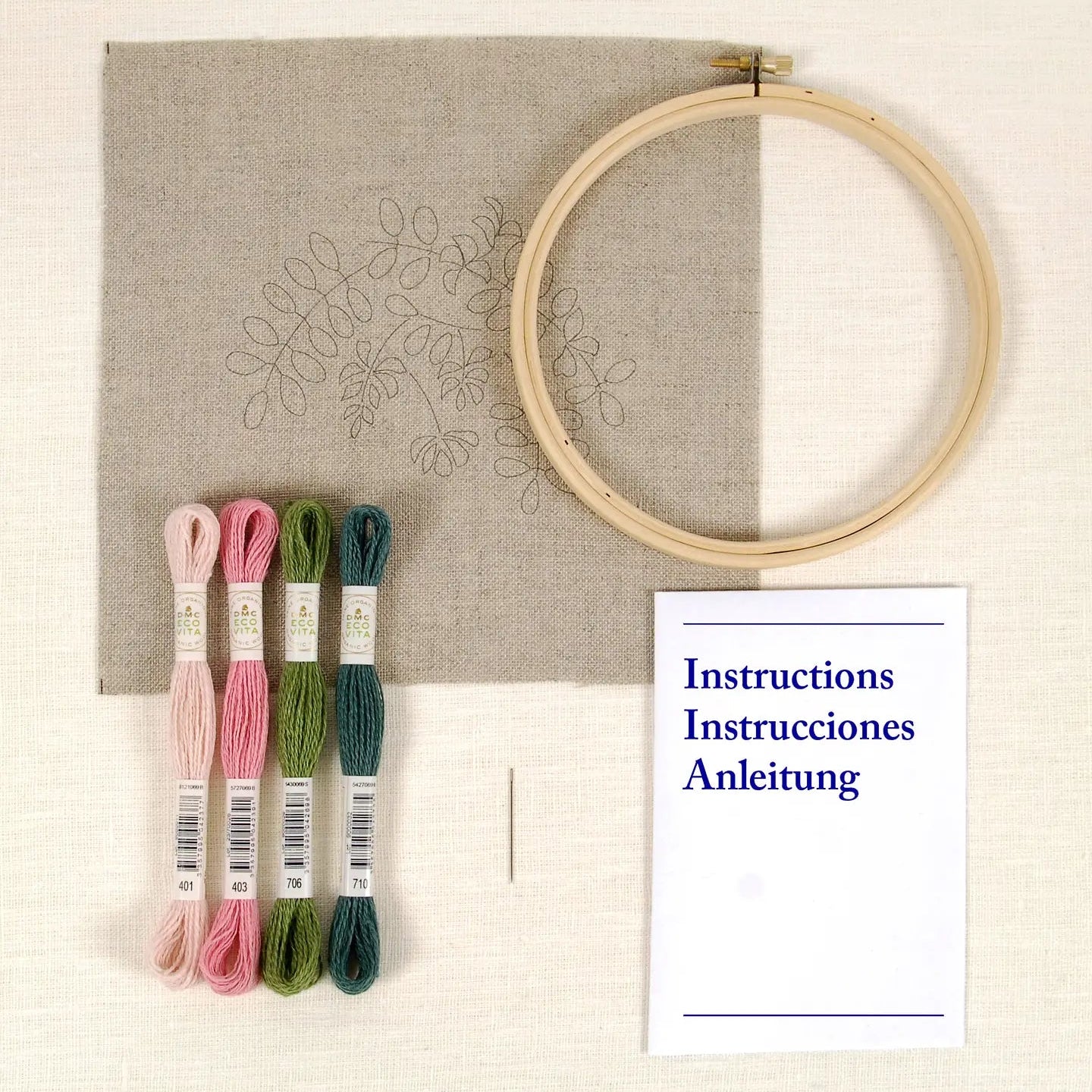 Embroidery hoop with fabric, threads, instruction sheet , and a needle on a cream background