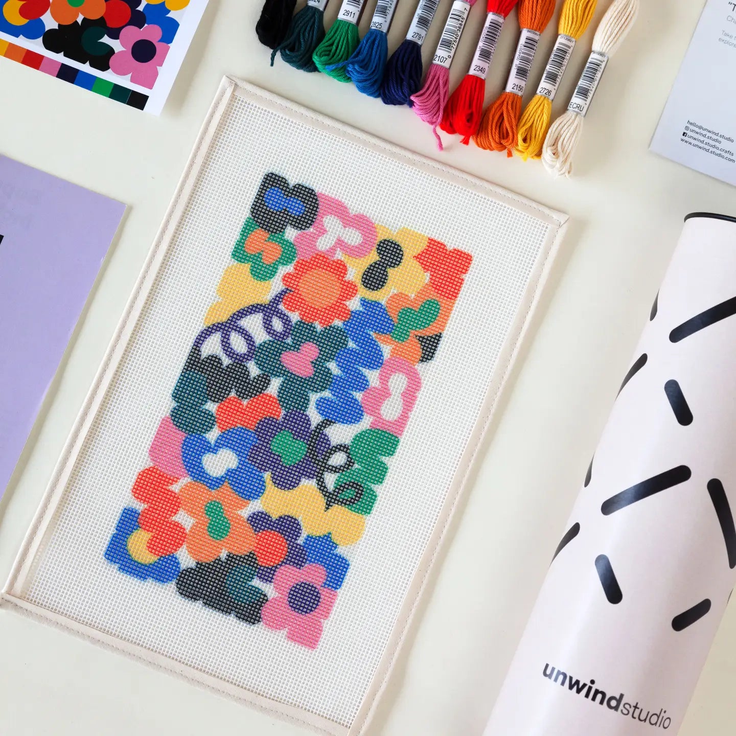 Close-up of some of the contents of a needlepoint kit with a vibrant Jungley Flowers design, including a printed canvas and a variety of coloured threads