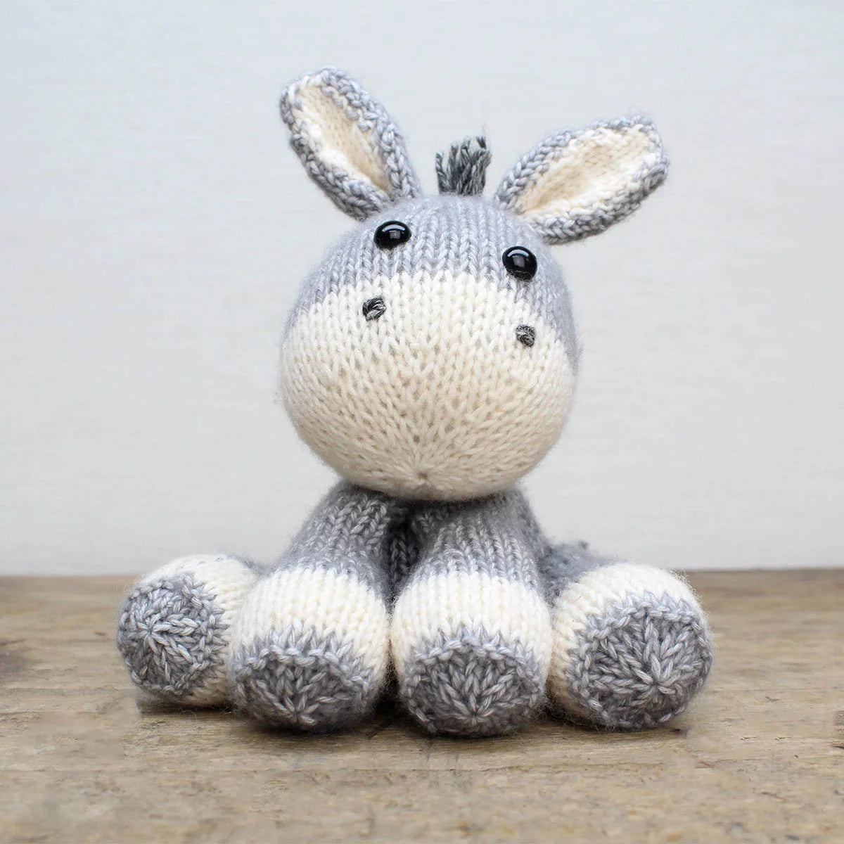 Knitted donkey soft toy on a wooden surface with a light grey background