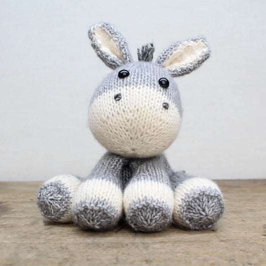 Knitted donkey soft toy on a wooden surface with a light grey background