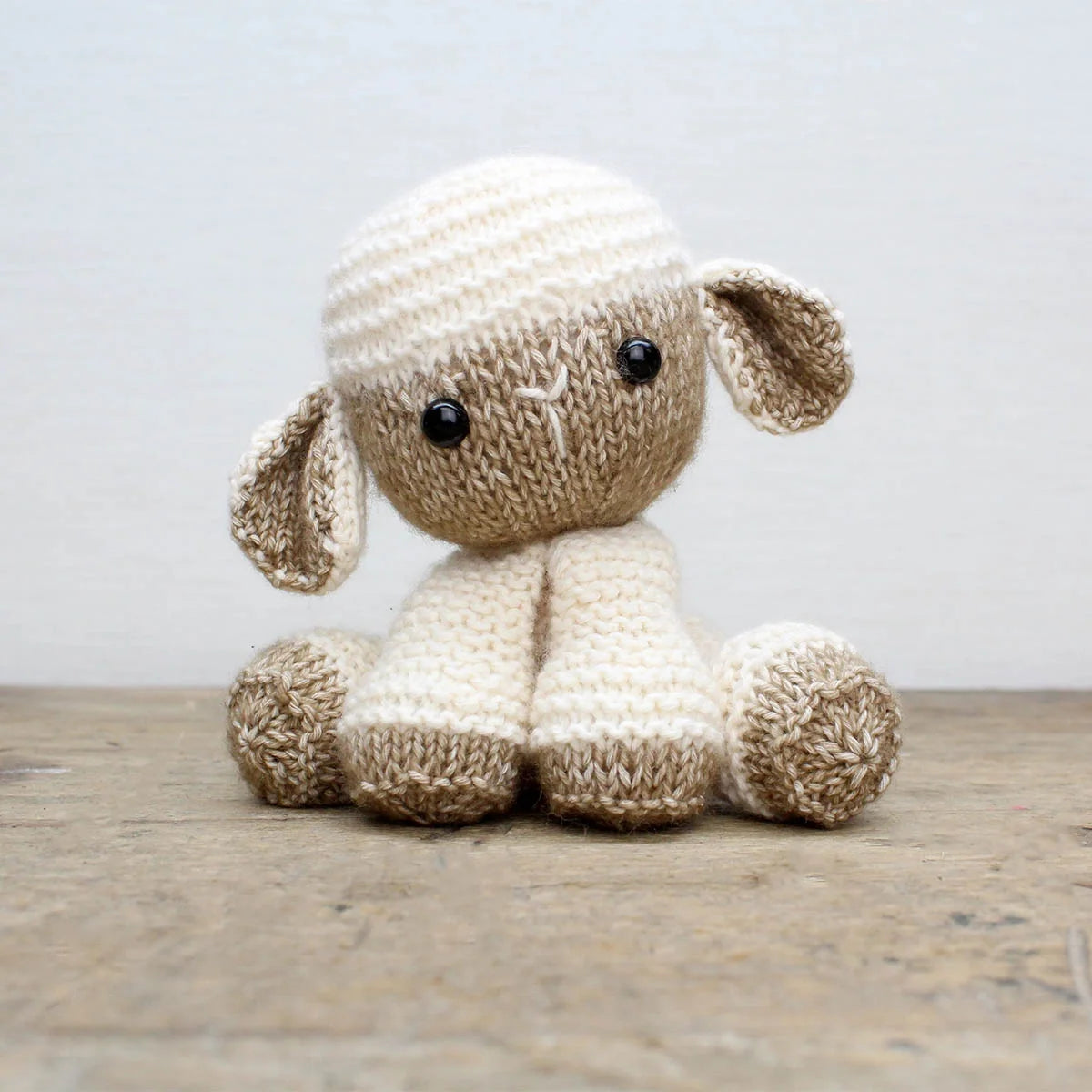 Knitted lamb soft toy on a wooden surface with a light background