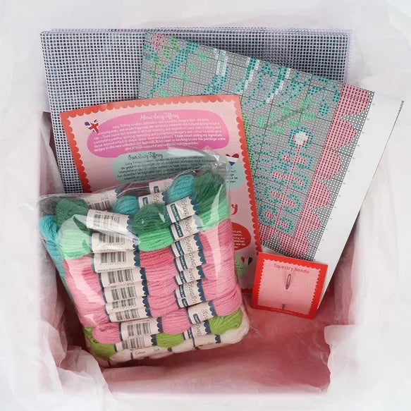 Cross-stitch kit with skeins of yarn, canvas fabric, and pattern chart on a white background