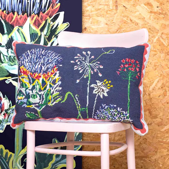 Decorative needlepoint cushion with floral design on a pink chair against a colourful background