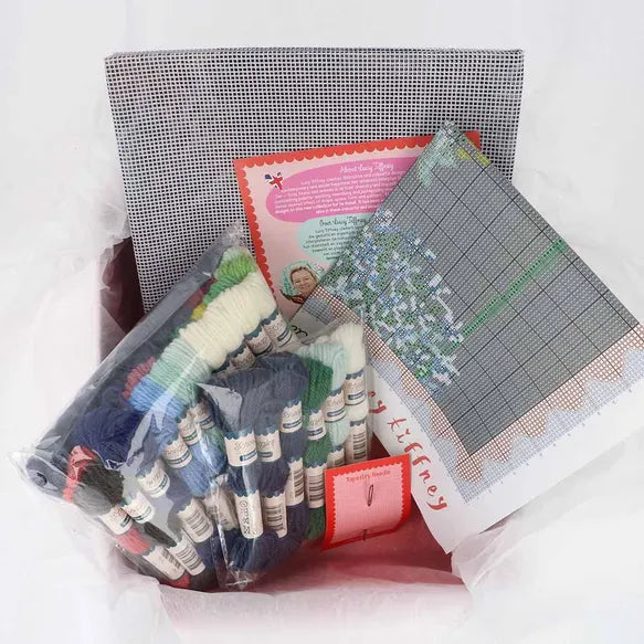 Cross-stitching kit with fabric, threads, and patterns on a white background