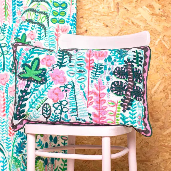 Floral and leaf patterned needlepoint cushion on a pink chair against a wooden wall
