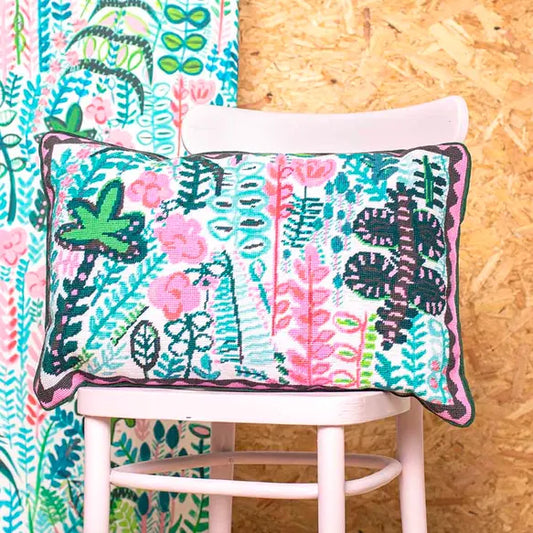 Floral and leaf patterned needlepoint cushion on a pink chair against a wooden wall