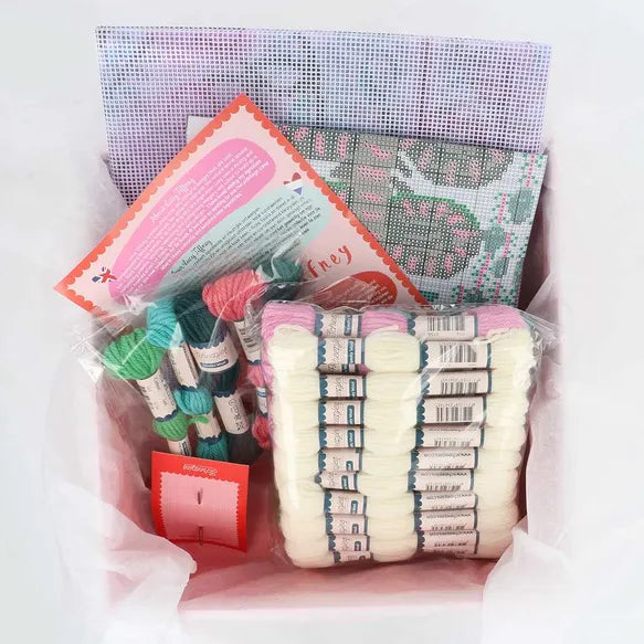 Packaged craft supplies including yarn skeins, needlepoint canvas, and a needle on a white background