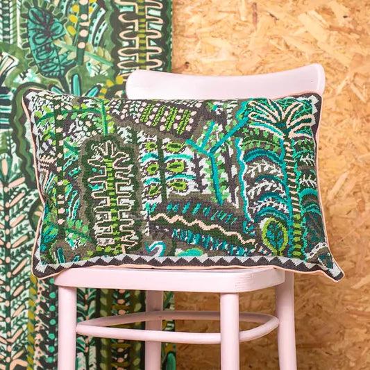 Decorative needlepoint cushion with green and blue botanical pattern on a chair against a wooden wall