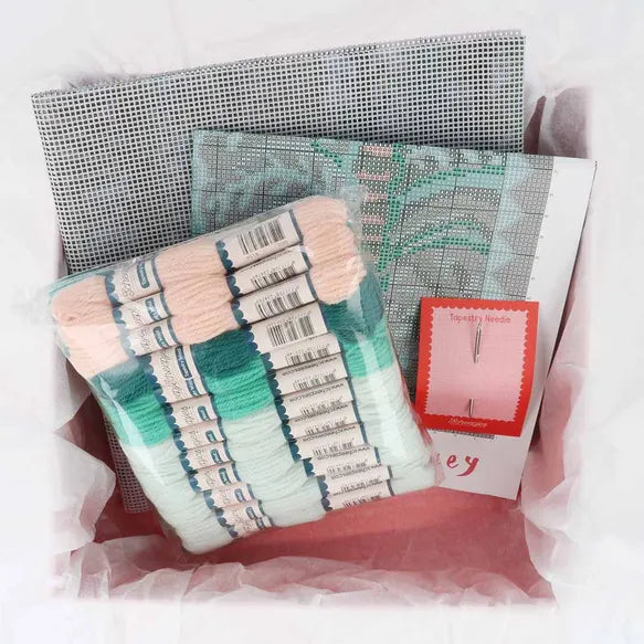 Packaged yarn with a patterned needlepoint canvas and a printed design card on a white background