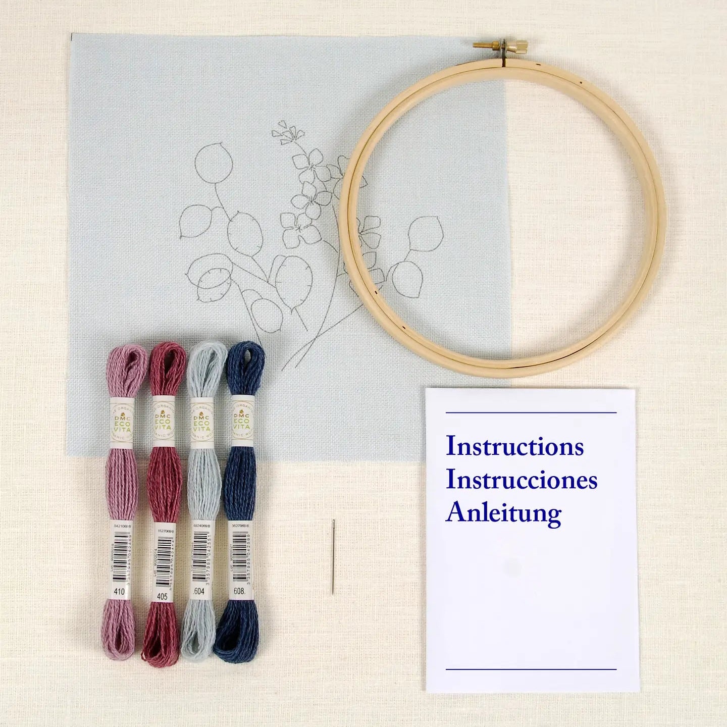 Embroidery hoop, threads, instructions, and a needle on a light background