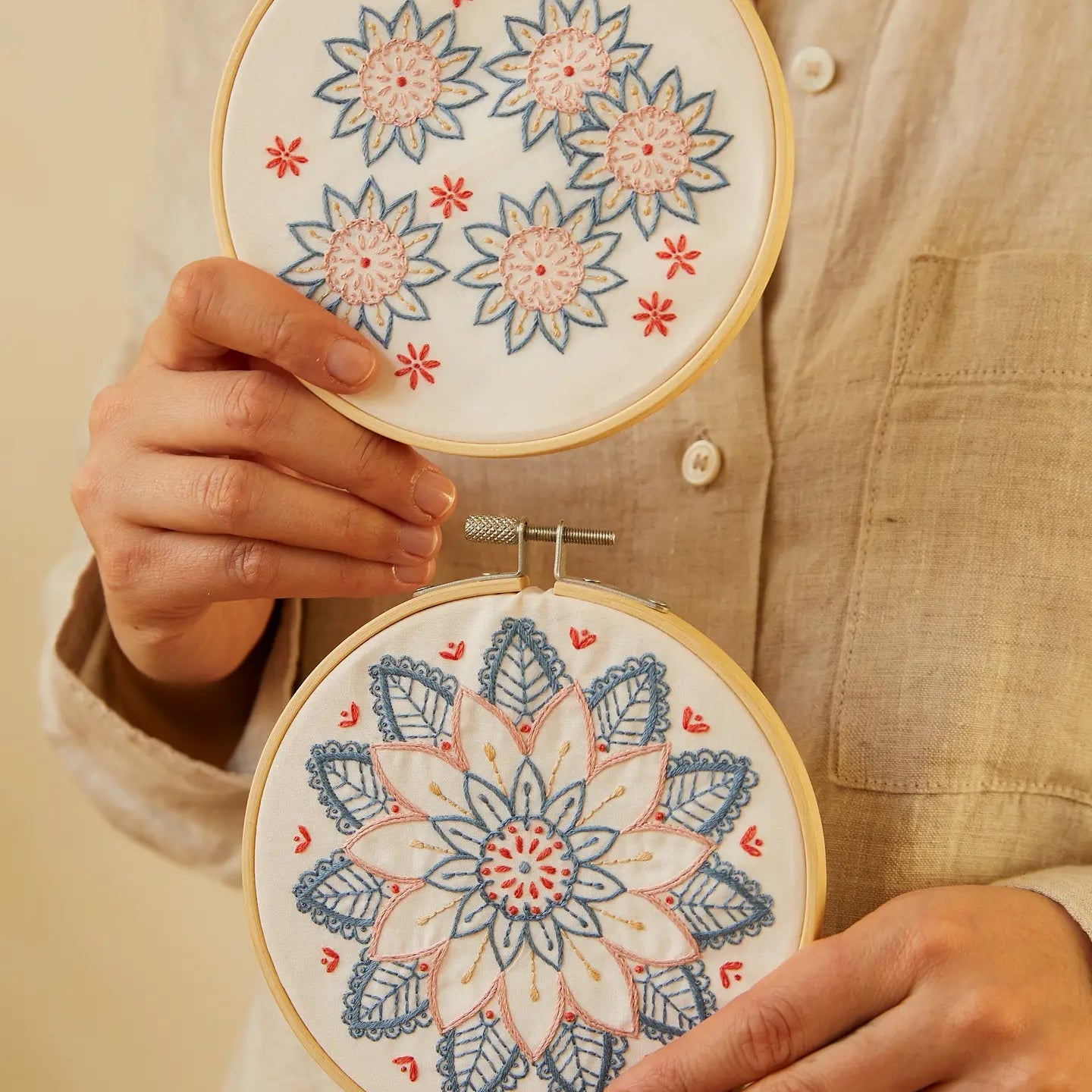 Person holding two embroidered hoops with mandala patterns on a light background