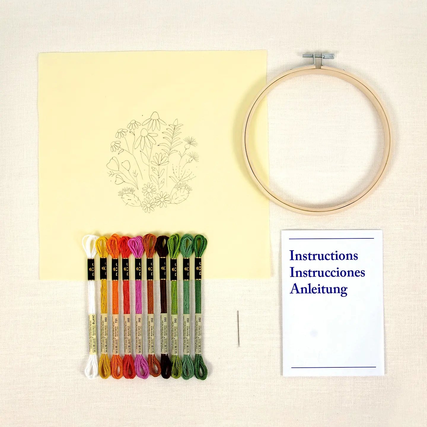 Embroidery  kit featuring printed design on fabric, a hoop with colourful threads and a instruction booklet on a light background