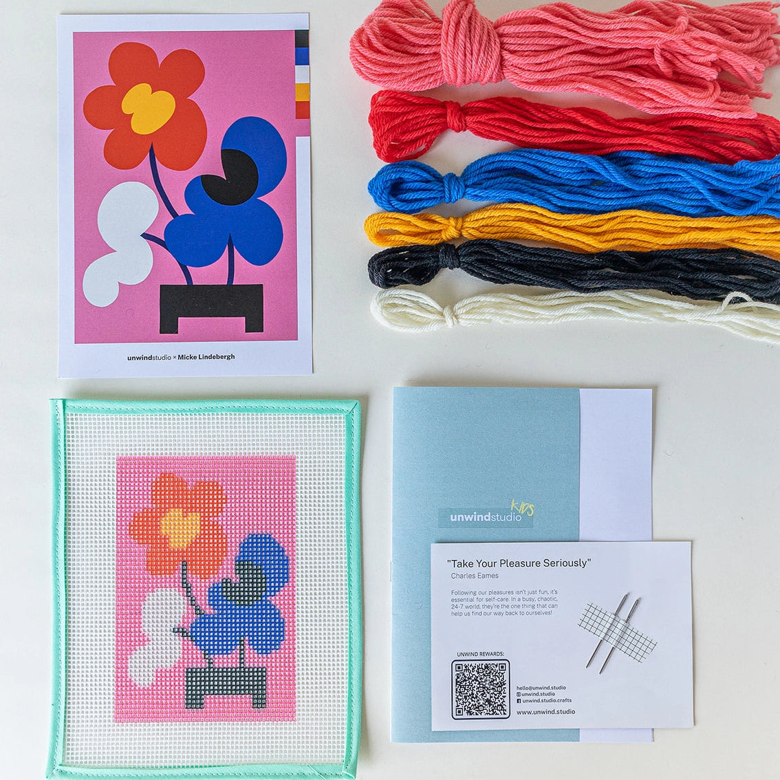 Contents of mickebana needlepoint kit, including printed canvas of an ikebana-inspired floral design, skeins of yarn, a photo of the original artwork, instruction booklet and needles