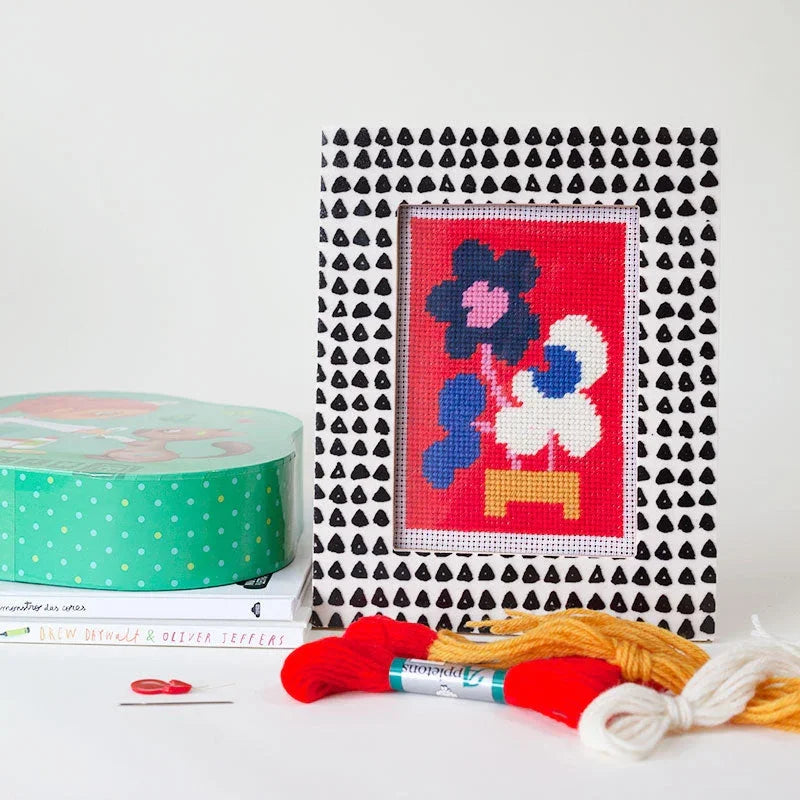 Framed cross-stitched artwork with colourful flowers on a white surface with crafting materials