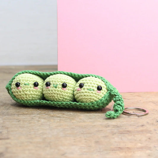 Crocheted keychain or bag charm featuring three peas in a pod in two shades of green on a wooden surface