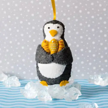 Small grey and white felt penguin decoration holding three yellow fish on a blue and grey background