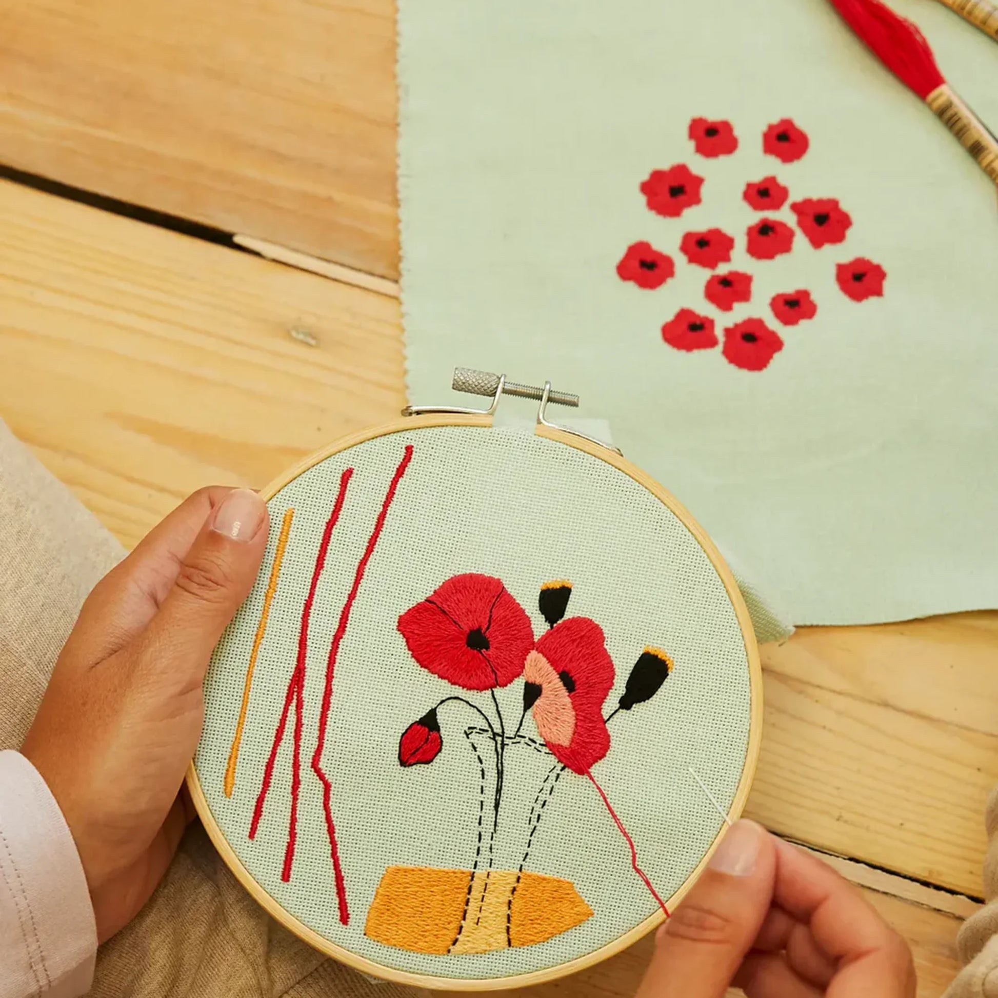 Completed red poppy embroidery in hoop with a coordinating floral design
 in background