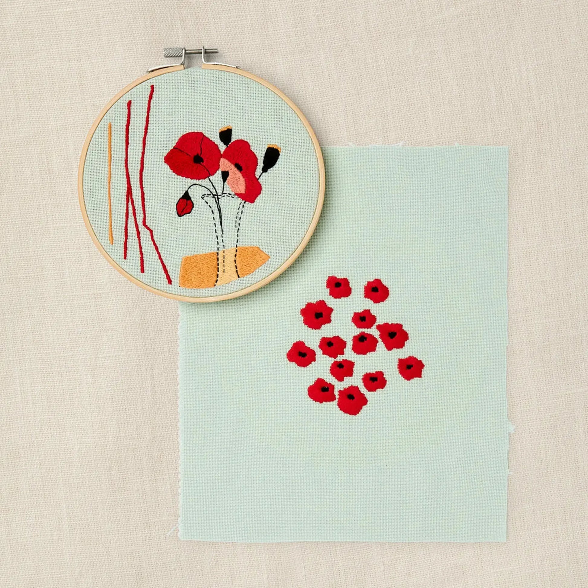 Embroidery hoop with red floral design with coordinating poppy pattern on a light blue fabric background