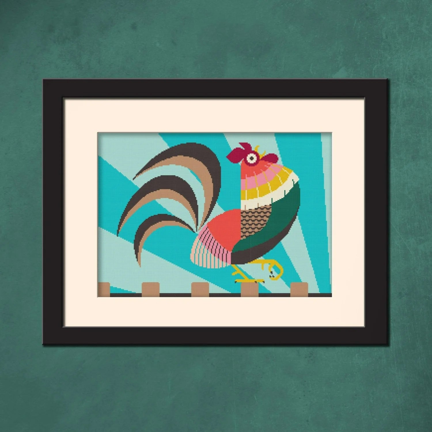Framed needlepoint artwork of a brightly coloured rooster displayed on a teal wall